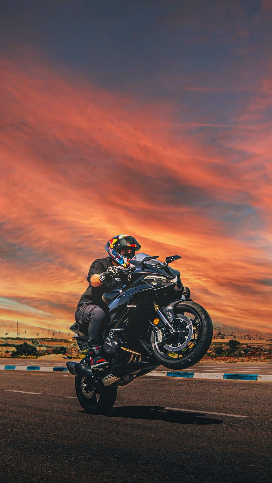Motorcyclist performing a wheelie against a dramatic sunset sky